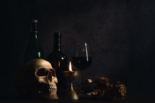 Still Life Of Humen Skull On Table With A Glass Of Wine And Wine Bottle In A Dim Light Room