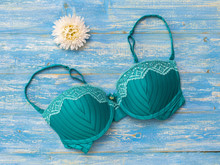 Green Bra With White Flower On Blue Wooden Background.