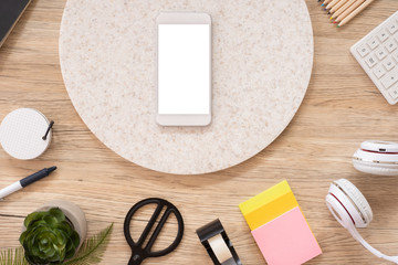 Poster - mobile mock up on office desk table top view with stationery,notebook,plant on wooden table background.smart phone screen for display of design.business object flat lay.clipping path device template