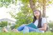 asian teenage reading a book while sitting in a park on a lawn with copy space
