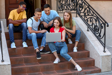 Wall Mural - Portrait of young students with laptop sitting on stairs outdoors