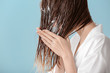 Beautiful young woman applying mousse on her hair after washing against color background