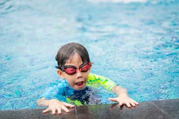 A boy is playing and swimming at the swimming pool in the evening.