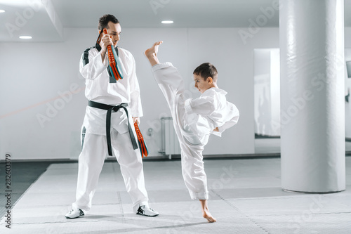 Fototapety Taekwondo  mlody-chlopiec-kaukaski-w-dobok-kopiac-boso-podczas-gdy-trener-trzyma-cel-kopniecia-taekwondo