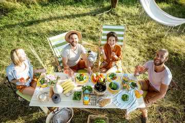 Wall Mural - Group of a young friends having festive lunch in the beautifully decorated garden on a summer afternoon, top view