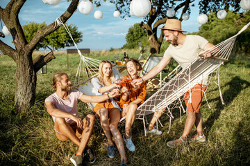 Wall Mural - Young friends relaxing with drinks on the backyard or garden with hammock during a festive meeting on the sunset