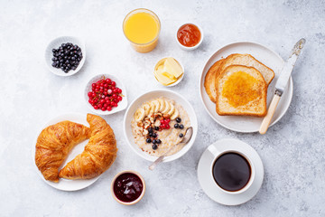 Wall Mural - Breakfast with oatmeal with berries and nuts, croissants, toasts with jam and butter, coffee and orange juice