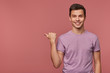 © timtimphoto - Young attractive cheerful guy wears in blank t-shirt, looks at the camera with happy expression, wants to turn your attention to copy space at the left side, stands over pink background.