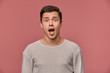 © timtimphoto - Young handsome shocked man in blank long sleeve, looks at the camera with with wide open mouth in surprised expression, isolated over pink background.