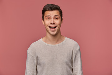 Portrait of cheerful handsome young guy wears in blank long sleeve, looks at the camera with happy expression, stands over pink background.