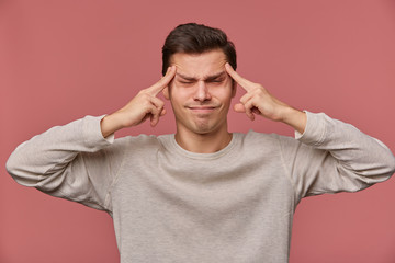 Poster - Photo of young attractive man in blank long sleeve, stands over pink background and shows headshot gesture with closed eyes, feels anhappy and migraineю