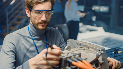 Poster - Professional Automotive Engineer in Glasses with a Computer and Inspection Tools is Testing an Used Electric Engine in a High Tech Laboratory with a Concept Car Chassis.