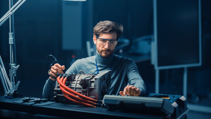 Poster - Professional Automotive Engineer in Glasses with a Computer and Inspection Tools is Testing an Used Electric Engine in a High Tech Laboratory with a Concept Car Chassis.