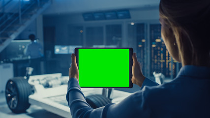 Poster - Female Engineer Holds a Tablet Computer with Green Screen Mock Up and Looks at Electric Car Chassis Prototype with Wheels, Batteries and Engine Standing in a High Tech Development Laboratory.