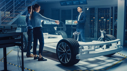 Poster - Automotive Design Engineers Talking while Working on Electric Car Chassis Prototype. In Innovation Laboratory Facility Concept Vehicle Frame Includes Wheels, Suspension, Engine and Battery.