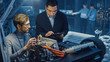 © Gorodenkoff - Two Professional Automotive Engineers with a Tablet Computer and Inspection Tools are Having a Conversation While Testing an Electric Engine in a High Tech Laboratory with a Concept Car Chassis.