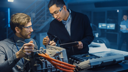 Fototapete - Two Professional Automotive Engineers with a Tablet Computer and Inspection Tools are Having a Conversation While Testing an Electric Engine in a High Tech Laboratory with a Concept Car Chassis.