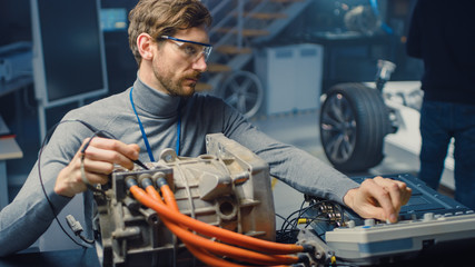 Poster - Professional Automotive Engineer in Glasses with a Computer and Inspection Tools is Testing an Used Electric Engine in a High Tech Laboratory with a Concept Car Chassis.