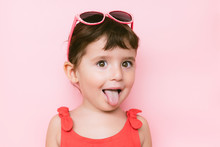 Portrait Of Little Girl Sticking Out Tongue In Front Of Pink Background