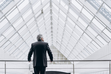 Serious elder man in big office centre thinking of future, investments and ideas. Shoot from the back