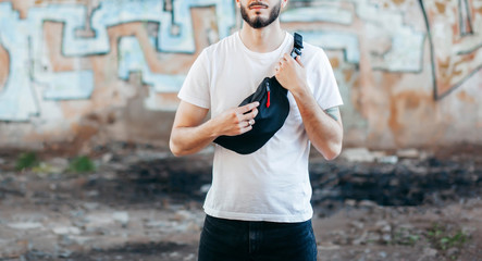 Canvas Print - Stylish bearded hipster in the at the city in a white T-shirt with waist bag