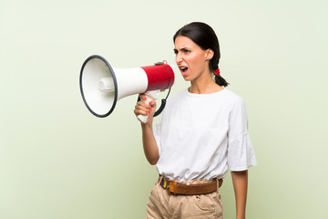 Young woman over isolated green background shouting through a megaphone