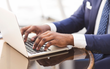 Black businessman typing something working on laptop in cafe, cropped