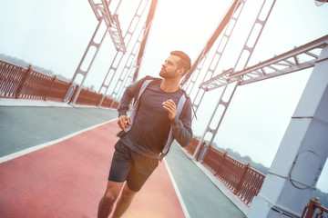 Healthy lifestyle. Young urban bearded man in sports clothing jogging on the bridge and looking aside