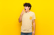 Young man over isolated yellow wall yawning and covering wide open mouth with hand