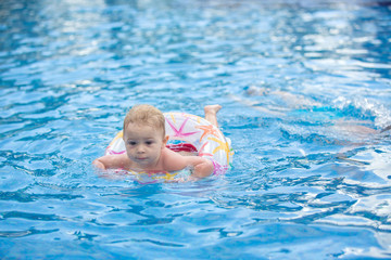 Wall Mural - Adorable happy little child, toddler boy, having fun relaxing and playing in a pool in inflatable ring on sunny day during summer vacation