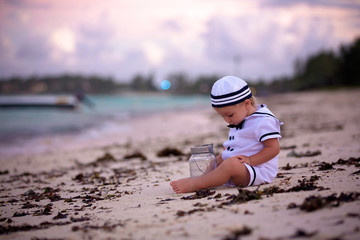 Poster - Beautiful toddler boy, dressed as a sailor, playing on the beach on sunset, enjoying tropical magical holiday vacation