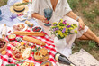 © Kate - Woman with glass of wine sit on chekered picnic blanket. Romantic outdoor picninc on green lawn