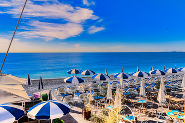 View to the beach of Nice; France, with sunshades, sunbeds, blue sea and sunshine.