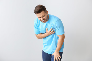 Young man suffering from heart attack on light background