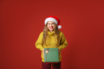 Beautiful young woman with Christmas gift on color background