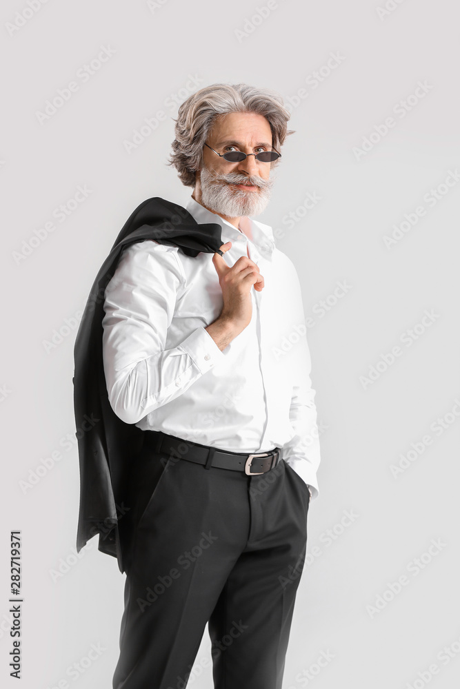 Fashionable senior man in stylish suit on light background