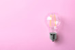 Vintage filament lamp bulb on pink background, top view. Space for text