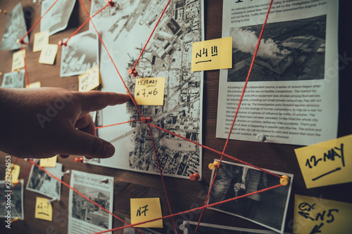 Detective board with photos of suspected criminals, crime scenes and evidence with red threads, selective focus