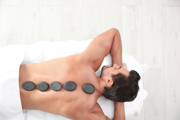 Poster - Young man receiving hot stone massage in spa salon, top view. Space for text