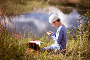 A Muslim child prays in nature near a beautiful lake.