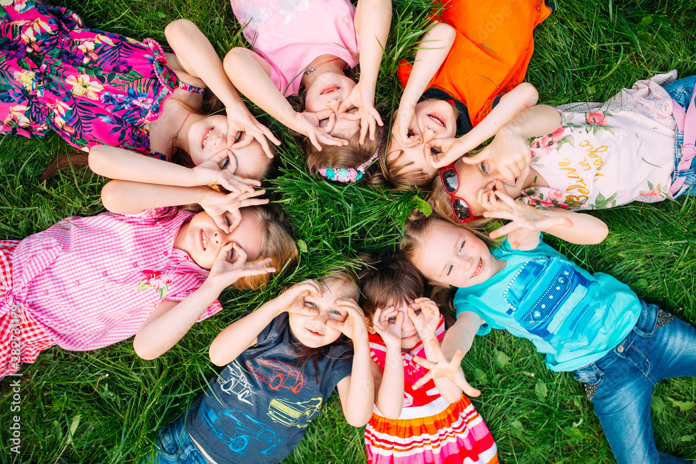 A group of children lying on the green grass in the Park. The interaction of the children. - obrazy, fototapety, plakaty 
