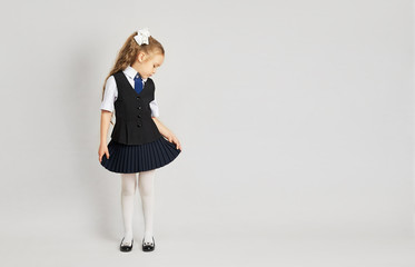 The little girl tried on a school uniform for the first time. A girl in a school uniform looks at herself from the side. Little girl in uniform on a white background.