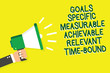Writing note showing Goals Specific Measurable Achievable Relevant Time Bound. Business photo showcasing Strategy Mission Man holding megaphone loudspeaker yelliw background speaking loud