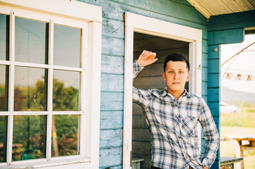 Outdoor portrait of handsome teenage boy wearing blue plaid shirt, leaning on the wall