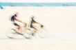 Two people riding bicycles at beach blurred motion