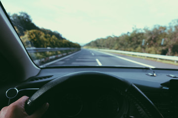 Inside view, hand of a driver on steering wheel of a car with empty asphalt road background. High-quality free stock image of driver hands on the steering wheel inside. Summer trip or vacation by car