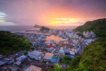 Wall Mural - Scenery of colorful sunrise at Yehliu, a fishing village on northern coast of Taipei, Taiwan, with view of a coastal highway along beautiful coastline & houses by the harbor under dramatic dawning sky