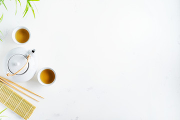 Asian tea concept, two white cups of tea and teapot surrounded with dry green tea  leaves , space for a text on white background. Brewing and Drinking tea.