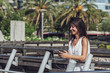 © Ruslan Grumble - Close-up portrait of cheerful young woman listening to the music on the phone. Beautiful girl over summer background with palm trees in the city. Gorgeous brunette lady enjoying the music outdoors.