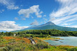 Panoramic view of Tierra del Fuego National Park, showing a volcano surrounded by green vegetation and water, against a blue sky.